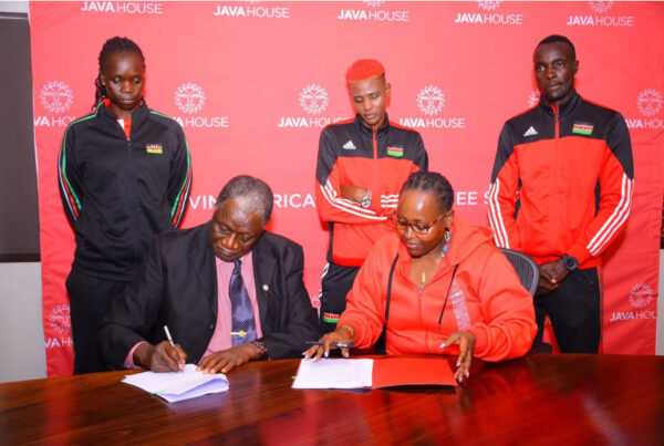 Java House CEO Priscilla Gathungu and Kenya Volleyball Federation President, Charles Nyaberi signing nutritional Sponsorship document with Malkia strikers standing behind them | Java Foundation